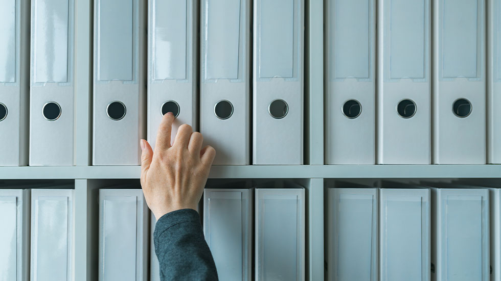 A hand reaching for a binder on a shelf.