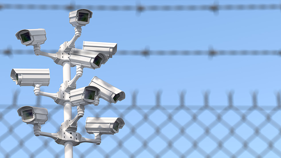 A tower of security cameras with barbed wire in the foreground.